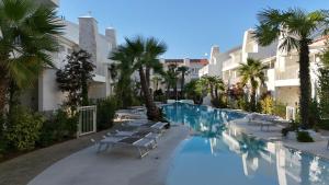 a swimming pool with lounge chairs and palm trees at VELORA STAYS Florinas in Lido di Jesolo
