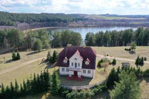 a small house on a field with a lake at Dworek Zielone Wzgórza Nad Jeziorem in Postawele