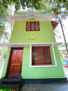 a green house with a clock on the front of it at Sandora Home Stay in Varkala
