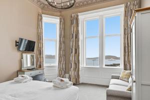 a bedroom with two beds and a tv and two windows at Corran House Guest House in Oban