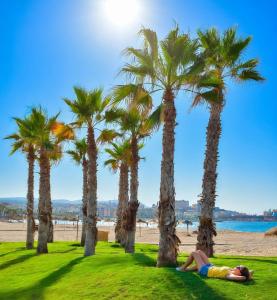 a woman laying on the grass under palm trees at the beach at Paseo del mar in Melilla