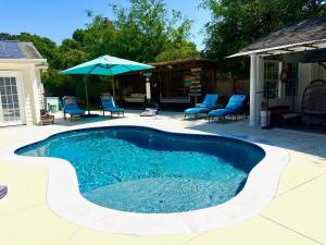 a swimming pool with blue chairs and an umbrella at Romantic Beach Style Cottage close to everything! in Whitehouse Plantation