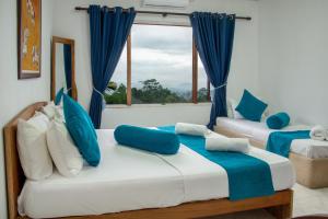 two beds in a room with blue curtains and a window at Bethel Rest Homestay in Kandy