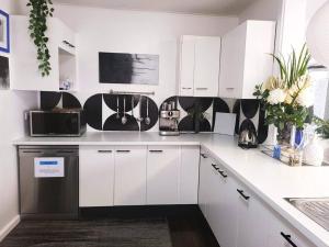 a kitchen with white cabinets and black and white appliances at Eleda House - Retro Hidden Gem in Cessnock