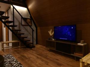 a living room with a television and a staircase at Chalé 4 Elementos Teresópolis - vista panorâmica e privacidade in Teresópolis