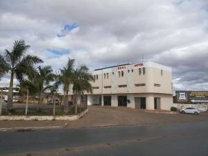 a white building with palm trees in front of a street at Hotel Real Trevo in Montes Claros