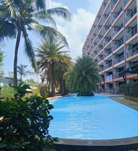 a large swimming pool with palm trees in front of a building at Cozy apartment with a sea view in Ban Bo Sai Klang