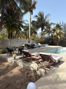 a pool with chaise lounges and a table and chairs at Villa Maria in Cap Skirring