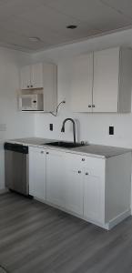 a white kitchen with a sink and white cabinets at Centennial Motel in Kindersley +28 photos