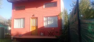 a red house with a door and a chair on a porch at Amapolas monoambiente in El Bolsón