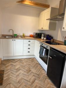 a kitchen with white cabinets and a wooden floor at Mini Treacle Cottage in Dundry +3 photos