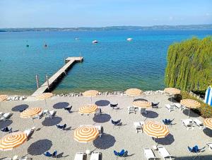 a beach with umbrellas and chairs and a dock at Hotel Tre Vele in Sirmione