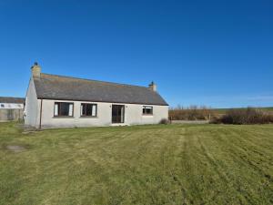 a white house with a large field in front of it at Quholmslie Farm Self-Catering in Stromness