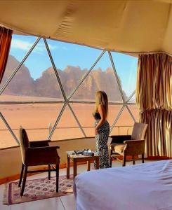 a woman standing in a room with a large window at Wadi Rum Nader Luxury Camp in Wadi Rum