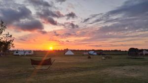 a sunset in a field with a tent and the sun at Bell-tent Rosa met uitzicht in Hensbroek