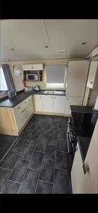 a kitchen with white cabinets and a black tile floor at Luxury 3 bedroom caravan hobourne Devon bay with hot tub in Goodrington
