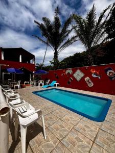 a swimming pool with white chairs and a red wall at Pousada N'ativaMar in Guaratuba