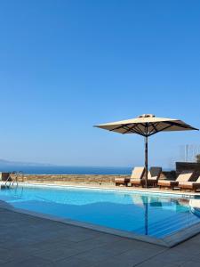 ein Swimmingpool mit Sonnenschirm und Liegestühlen und das Meer in der Unterkunft August Andros in Ándros