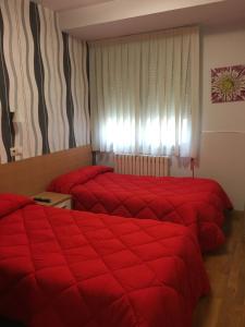two beds in a hotel room with red comforter at Hostal La Cortijana in Logroño