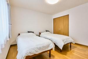 two beds in a room with white sheets at Furano Noie in Furano