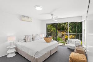 a white bedroom with a bed and a chair and a window at Searene By The Sea in Airlie Beach