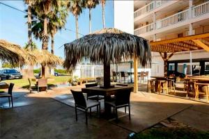 a patio with a table and chairs under a straw umbrella at The Sandbar Stay - North Beach Waterfront Condo in Corpus Christi