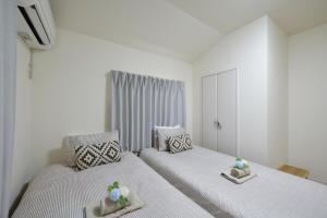 two beds in a room with white walls at Aiki No Yado-Kokuba- in Naha