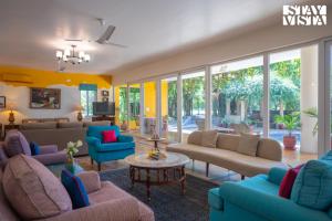 a living room with couches and tables and windows at StayVista at The Hideout Farms with Lawn and private Pool in Kurukshetra