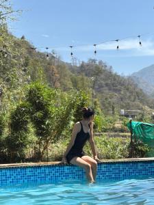 a woman sitting on the edge of a swimming pool at Sukoon in Nainital