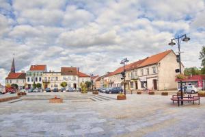 a town square with buildings and a street with cars at Cisza nad Kalwą in Pasym +5 photos