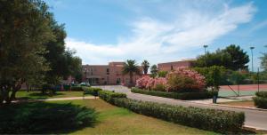 a street in front of a building with trees and flowers at VOI Florio Resort in Cinisi