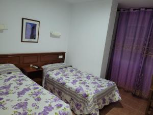 two beds in a room with purple curtains at Hostal La Perla in Zalamea de la Serena