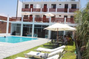 un hôtel avec une piscine, un parasol et des chaises dans l'établissement Hotel Residencial Los Frayles, à Paracas