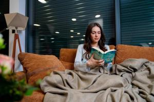 a woman sitting on a couch reading a book at Villa Aurora mit Sauna und Whirlpool in Dranske
