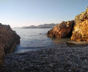 a rocky beach next to the water with mountains at Louis Studios Armeos in Masouri