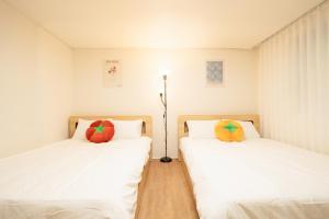 two beds in a room with white sheets and colorful pillows at Banghwa Space 5 min to Banghwa Stn, Near Gimpo Airport, Magok & COEX in Seoul