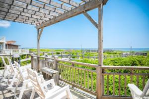 a deck with white chairs and a view of the ocean at Beach Buzz by Oak Island Accommodations in Caswell Beach