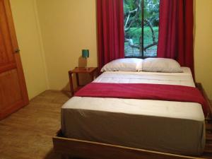 a bedroom with a bed with red curtains and a window at Suites Chile Verde in Manzanillo