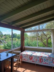 a room with a bed and a table and windows at Miralrio in Santa Rosa de Calamuchita