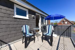 two chairs and a table with an umbrella on a balcony at Pension Sielmöwe in Neuharlingersiel