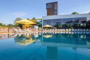 a pool of water with chairs and umbrellas in front of a building at Aquasolis Spa Hotel in Poľný Kesov