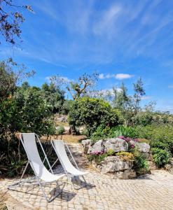 two white chairs sitting next to some rocks and flowers at Casa dos amigos in Chão de Couce