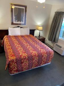 a bedroom with a large bed with a red and orange blanket at Crystal Motel in Red Bluff