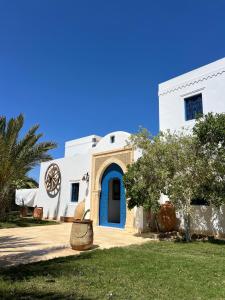 a white house with a blue door and a yard at Houch Ennejma, Chambres d'hotes, Spa et bien être in Al Ḩārah al Kabīrah