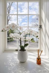 a white vase with white flowers in front of a window at Yarwell Mill in Nassington