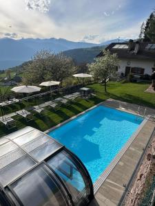 a pool with chairs and umbrellas and a house at Alpenrose in Meltina