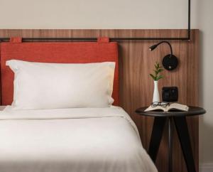 a bed with a red headboard and a table with a lamp at Intercity Porto Alegre Praia de Belas in Porto Alegre
