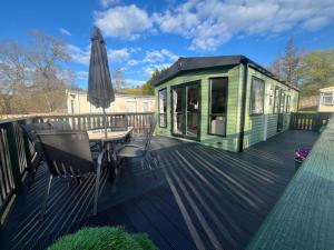 a green house with a table and an umbrella on a deck at Snug on the Teviot in Hawick