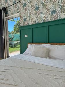 a bed with a green headboard next to a window at Backyard Cottage in Răhău