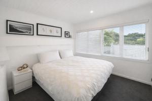 a white bedroom with a bed and a window at Raglan West Cottage, Surf Side Escape in Raglan